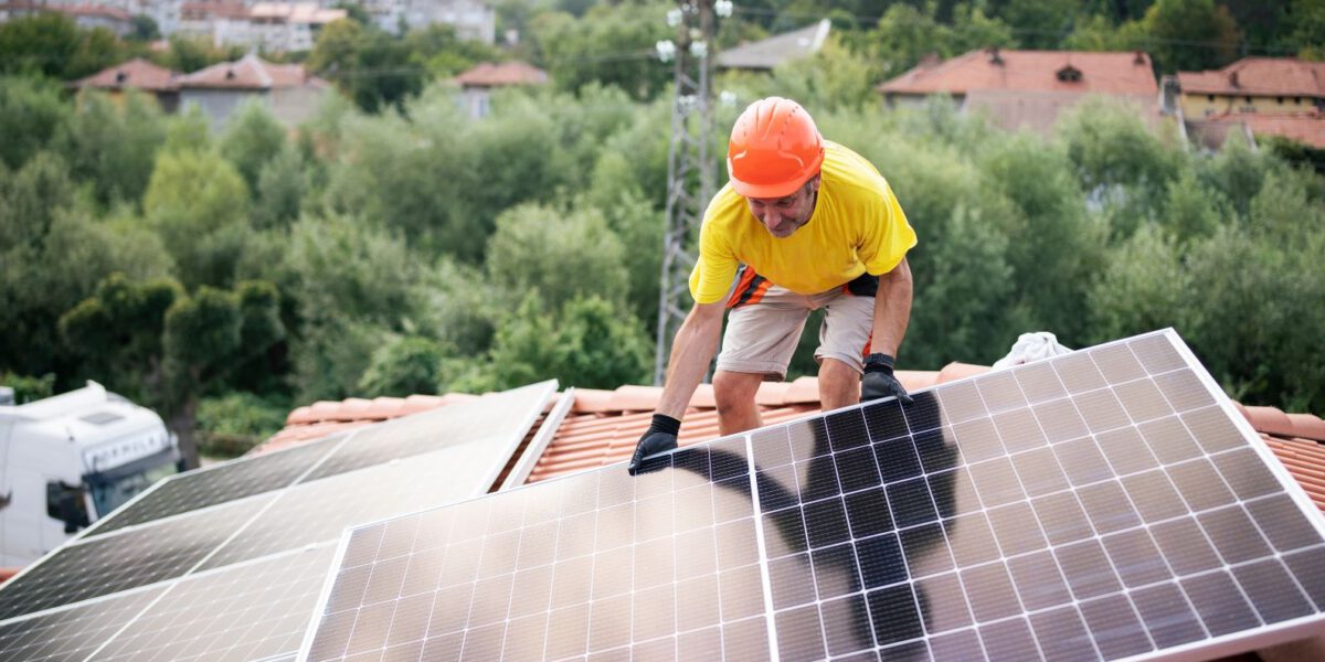 Instalator w rękawiczkach i kasku montuje panele słoneczne na dachu pokrytym dachówką, korzystając z zerowej stawki VAT na montaż fotowoltaiki w Niemczech.