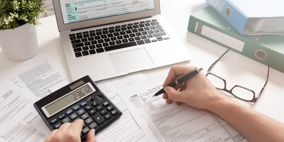 Biurko z dokumentami podatkowymi, laptopem, kalkulatorem i osobą wypełniającą formularze podatkowe, przygotowującą wniosek o Freistellungsbescheinigung.
